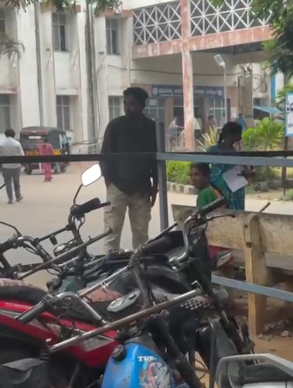 రోడ్డు పక్కన నిలబడి ఉన్న వ్యక్తి, కూర్చున్న మహిళలు; నేపథ్యంలో వాహనాలు